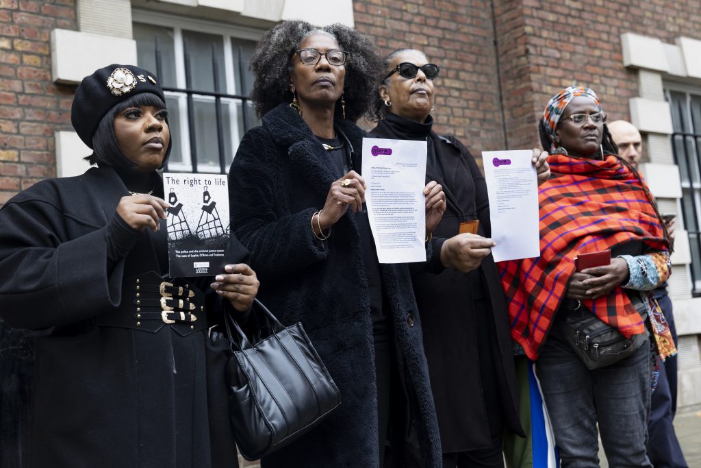 4 women stand together in a row - 3 of them (from left to right Sheeda Nzumba Kibala, Marcia Rigg and Susan Alexander) dressed in all black, and the 4th (Kadija George) wrapped in a Kenyan Masaai blanket. 2 hold up the 2 sheets of a letter bearing the UFFC old logo, and one holds a leaflet titled "The Right To Life"